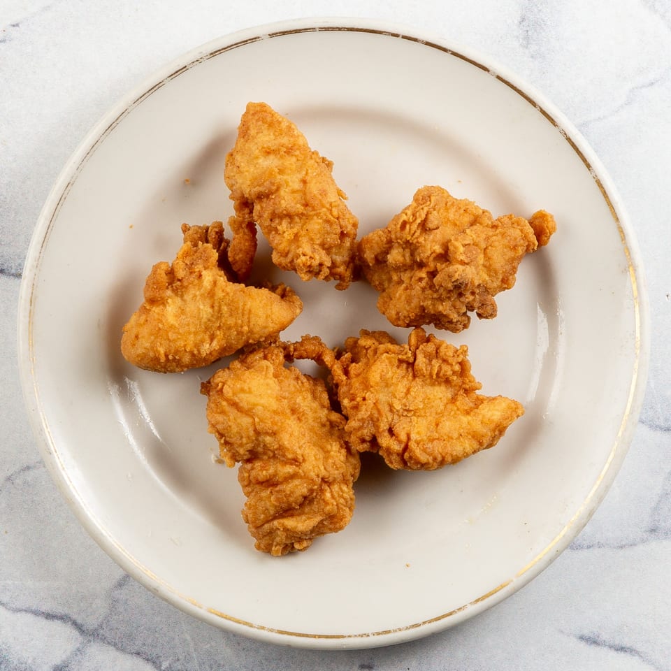 Five golden-brown fried chicken pieces arranged on a white plate with a gold rim.
