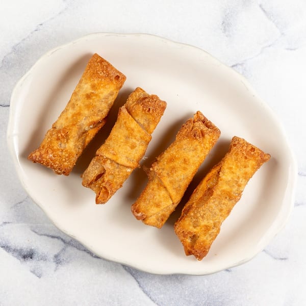 Four golden-brown fried egg rolls arranged on a white, irregularly shaped plate against a marble background.