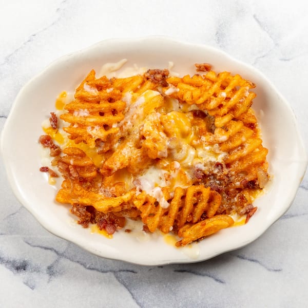 Waffle fries loaded with melted cheese and ground meat in a white bowl on a marble surface.