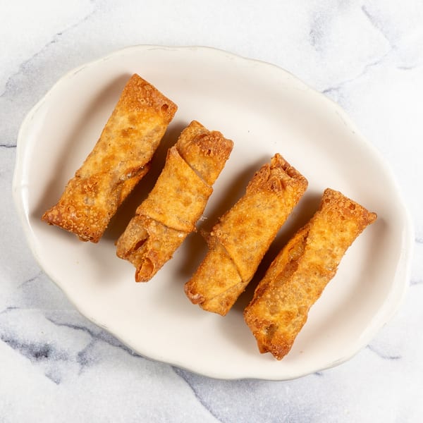 Four golden-brown, crispy egg rolls arranged on a white, irregularly shaped plate.