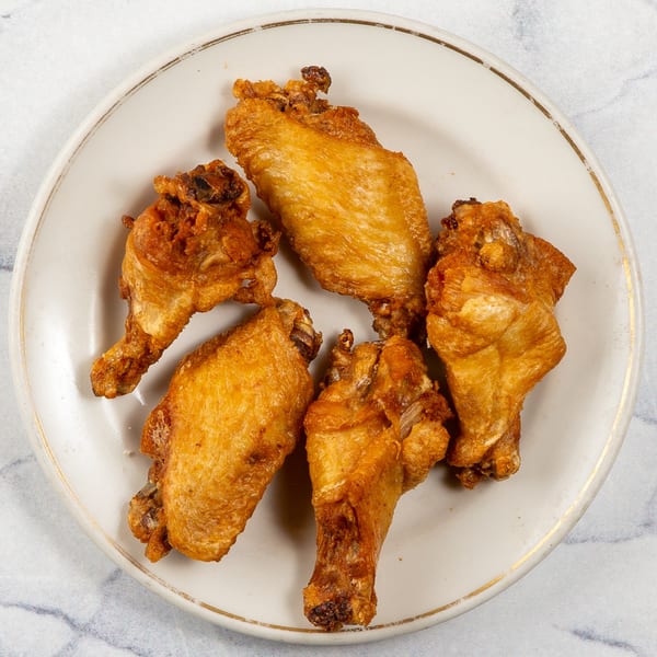 Five crispy, golden-brown fried chicken wings arranged on a white plate with a gold rim.