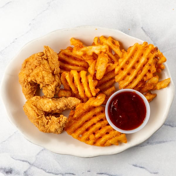 Crispy chicken tenders and waffle fries with a side of dipping sauce on a white plate.