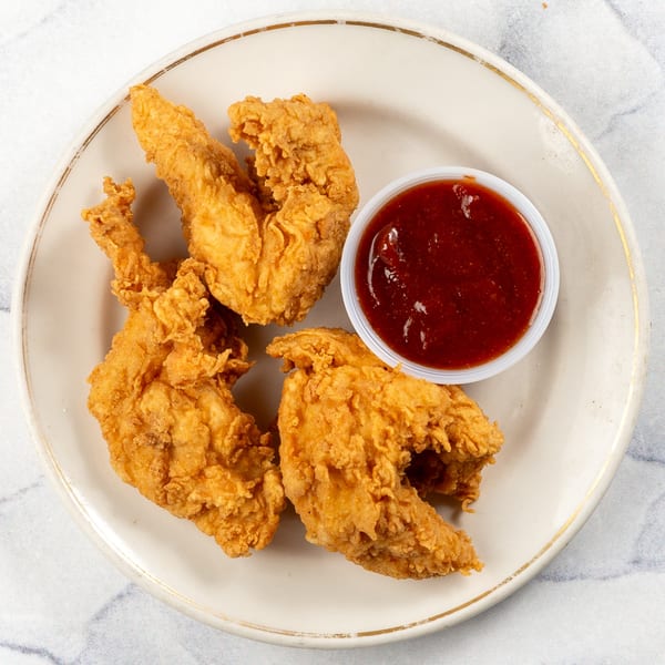Three crispy fried chicken tenders with a side of dark red dipping sauce on a white plate.