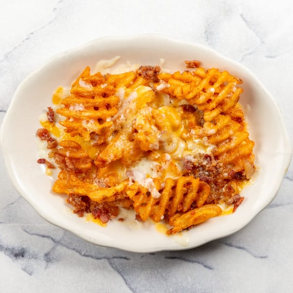 Waffle fries covered in melted cheese and ground meat, served in a white bowl.
