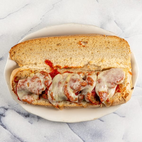 Mike N' Dangelo's meatball sub with melted mozzarella cheese and marinara sauce on a white plate.