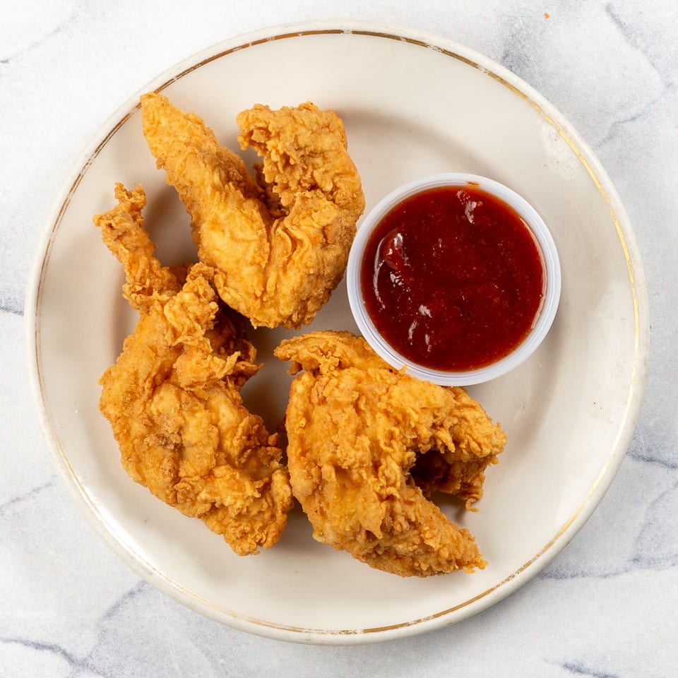 Crispy fried chicken tenders with a side of red dipping sauce on a white plate.