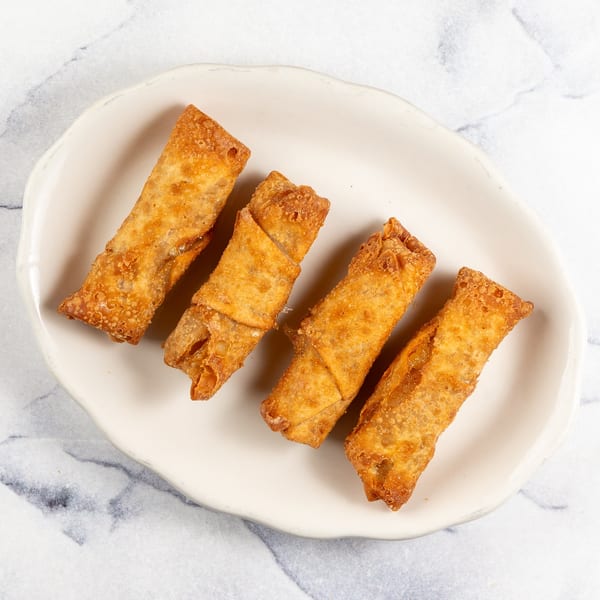 Four crispy, golden-brown egg rolls arranged on a white, irregularly shaped plate.