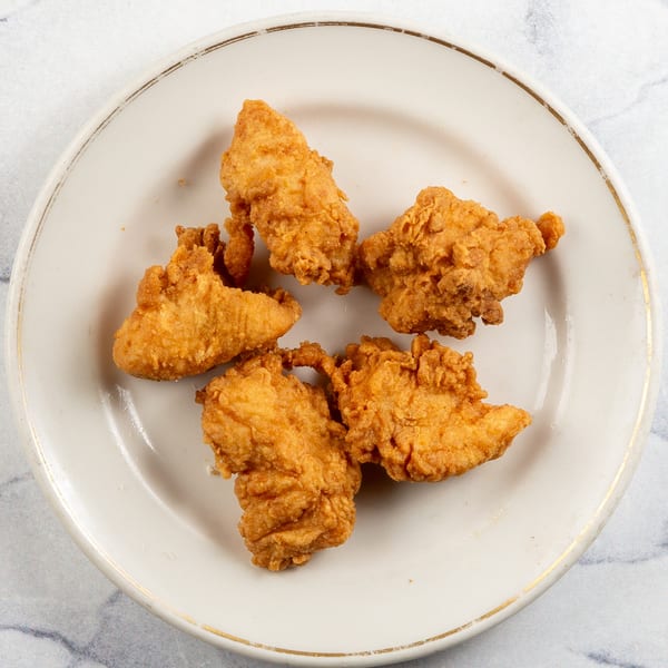 Five golden-brown fried chicken tenders on a white plate with a gold rim.