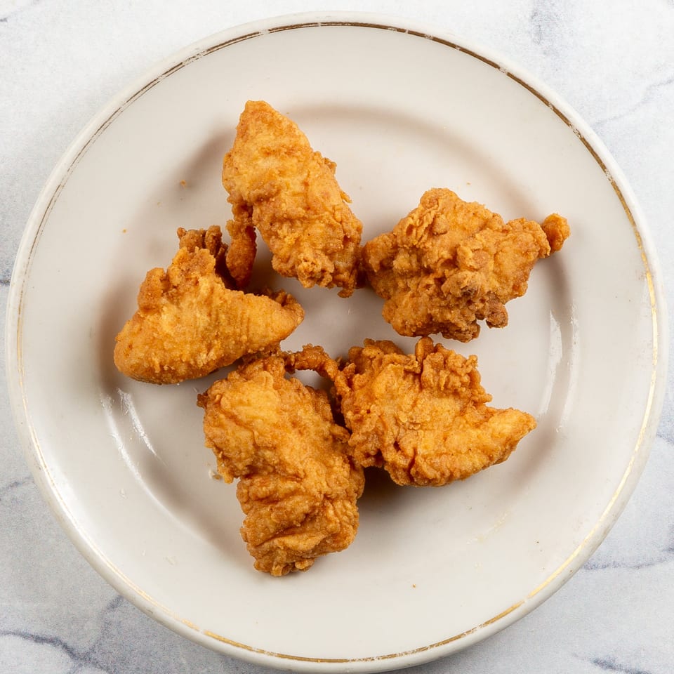 Five golden-brown fried chicken tenders on a white plate with a gold rim.