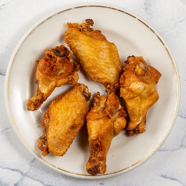 Five crispy, golden-brown chicken wings arranged on a white plate with a gold rim.