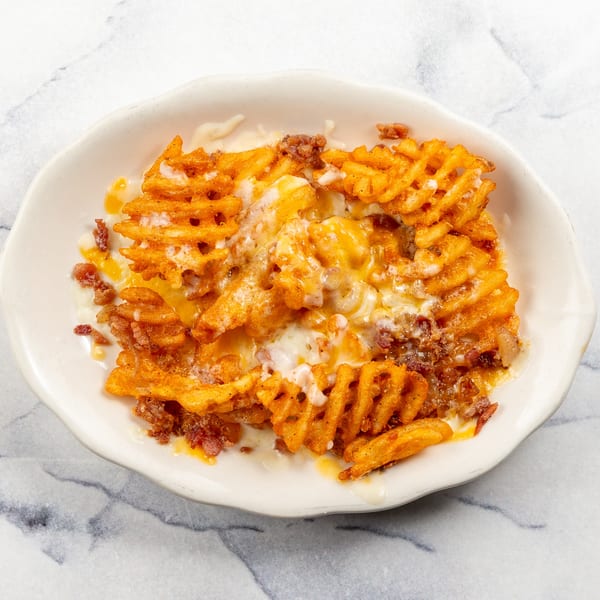 A white bowl filled with golden waffle fries, melted cheese, and ground meat on a marble surface.
