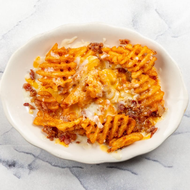 A white bowl filled with golden waffle fries, melted cheese, and ground meat on a marble surface.