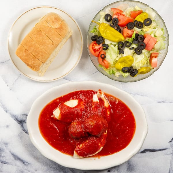 Stuffed shells with meatballs and red sauce, a side salad, and sliced bread on a marble surface.