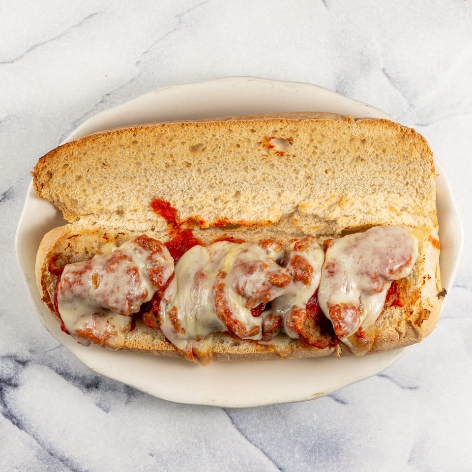A meatball sub with melted cheese and marinara sauce on a white plate, from Mike N' Dangelo's.