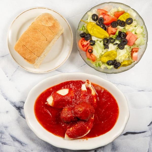 Stuffed shells with meatballs and red sauce, a side salad, and sliced bread on a marble surface.