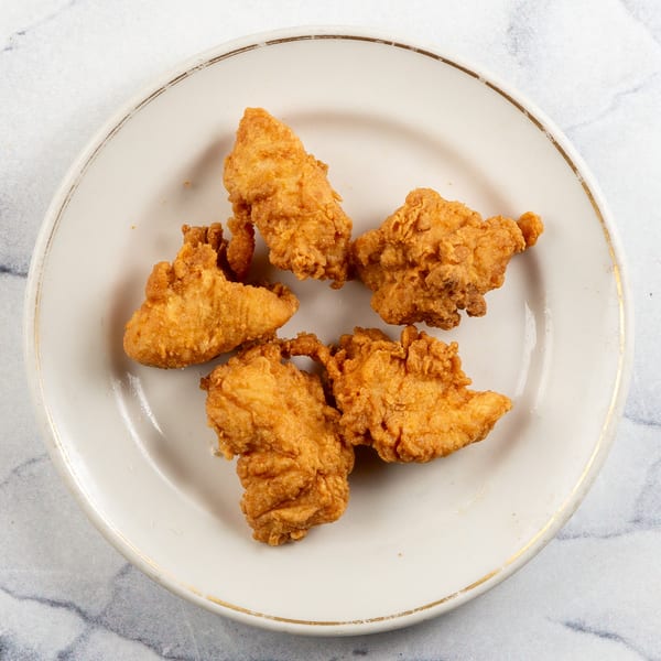 Five golden-brown fried chicken tenders arranged on a white plate with a gold rim.